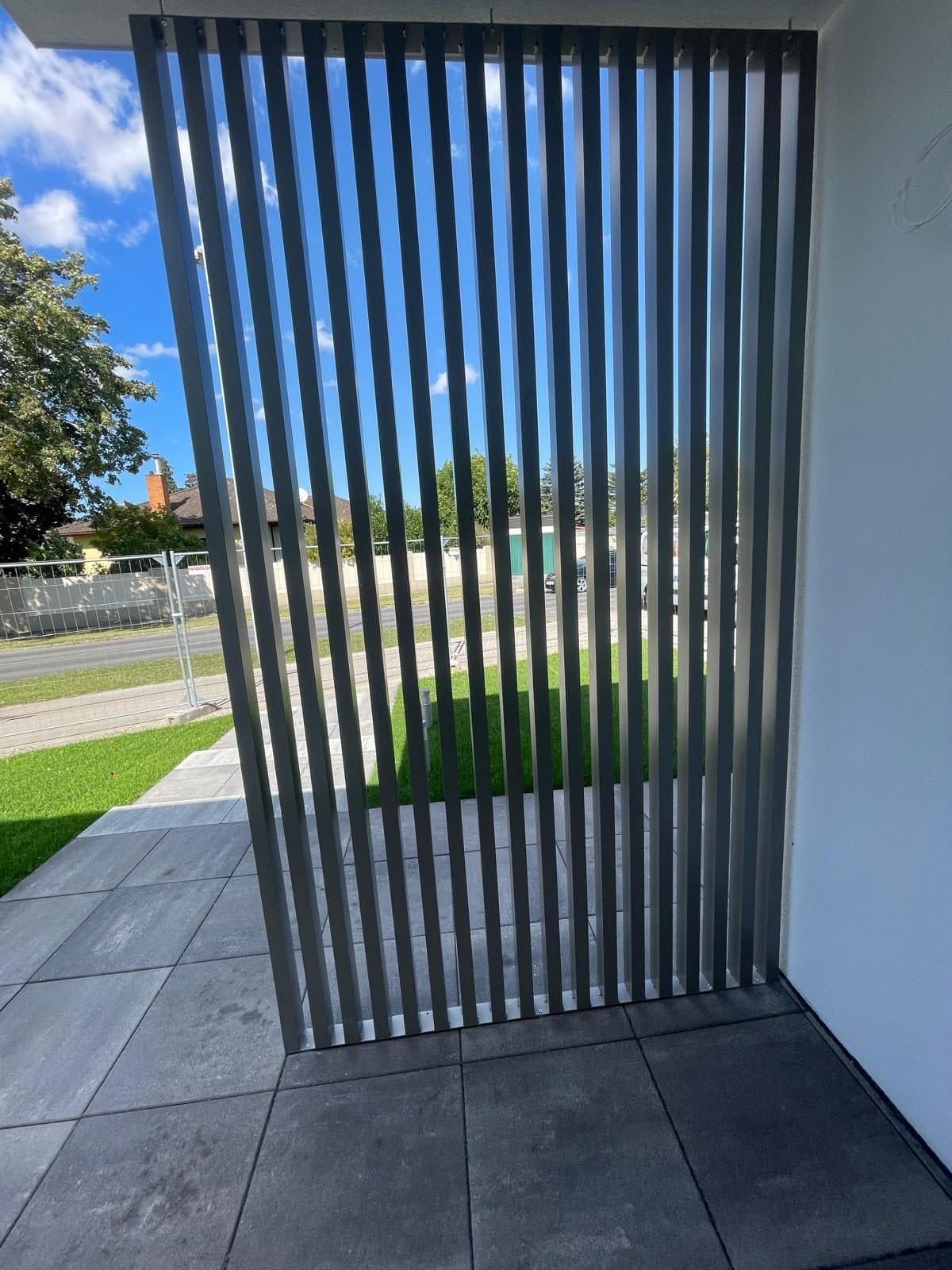 Nahaufnahme vertikaler Aluminiumlamellen vor dem Garten