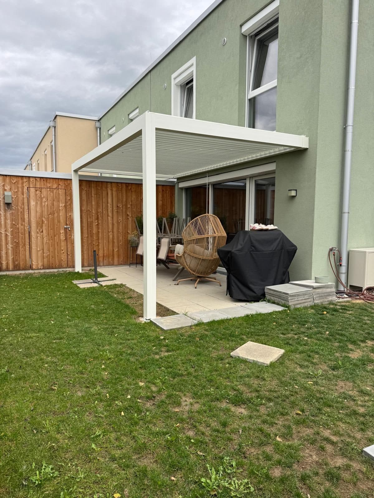 Weißes Lamellendach über einer kleinen Terrasse an einem Reihenhaus