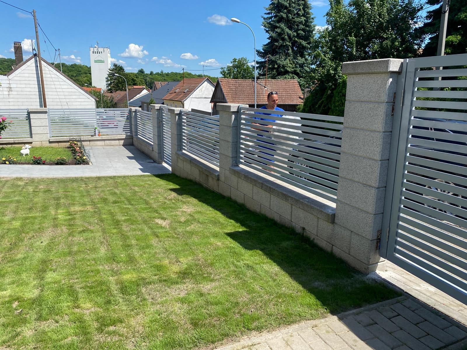 Hellgrauer Lamellenzaun mit Steinpfeilern entlang eines Rasens