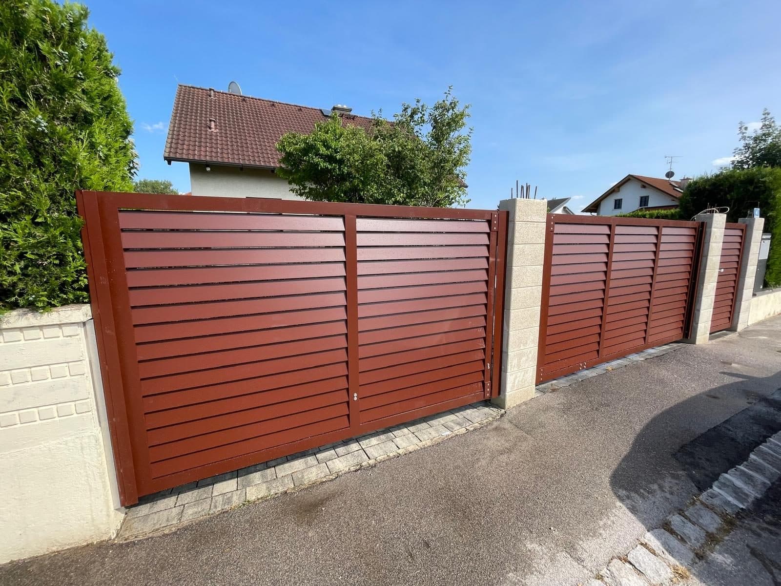 Rotbrauner Lamellenzaun mit Pfeilern entlang einer Straße